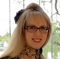 Portraitfoto einer Person mit langen Haaren, Brille und Schmuck im Haar, die in die Kamera lächelt