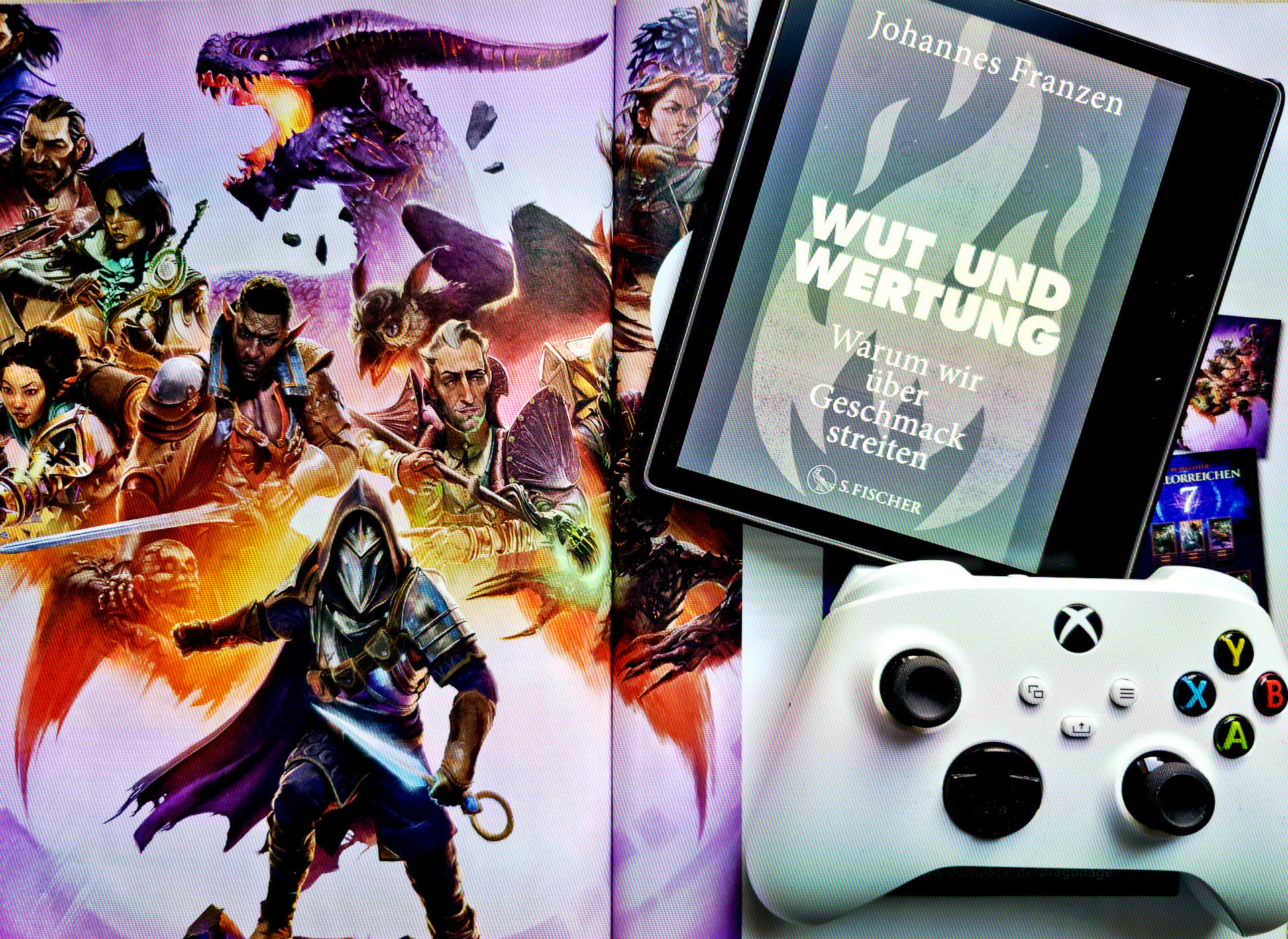 Ein eBook-Reader und ein Game Controller liegen auf einer Spielezeitschrift; in der Zeitschrift ist ein Artwork zum Spiel Dragon Age Veilguard zu sehen